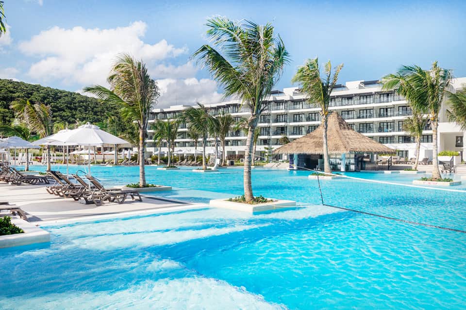 Luxury resort pool with palm trees, loungers, and modern white building architecture