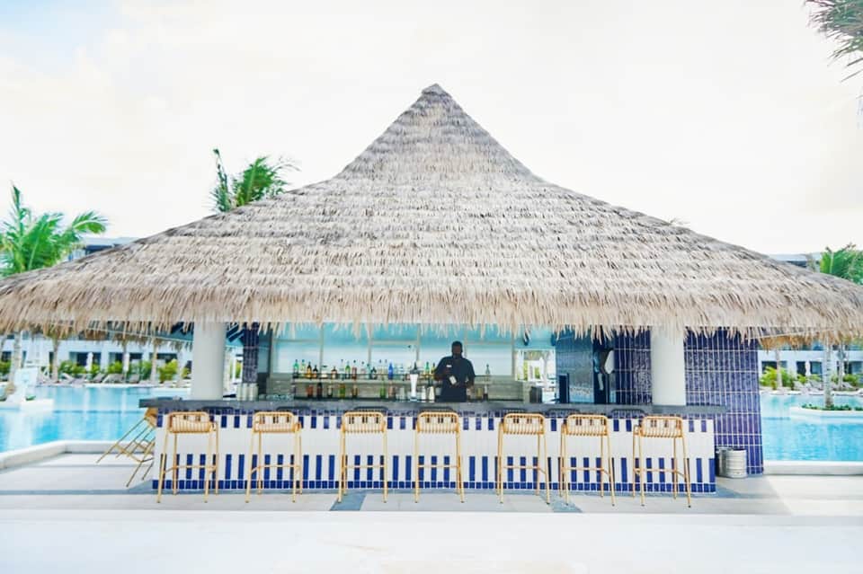 Beachfront bar with thatched roof, blue and white striped seating, and pool overlooking ocean