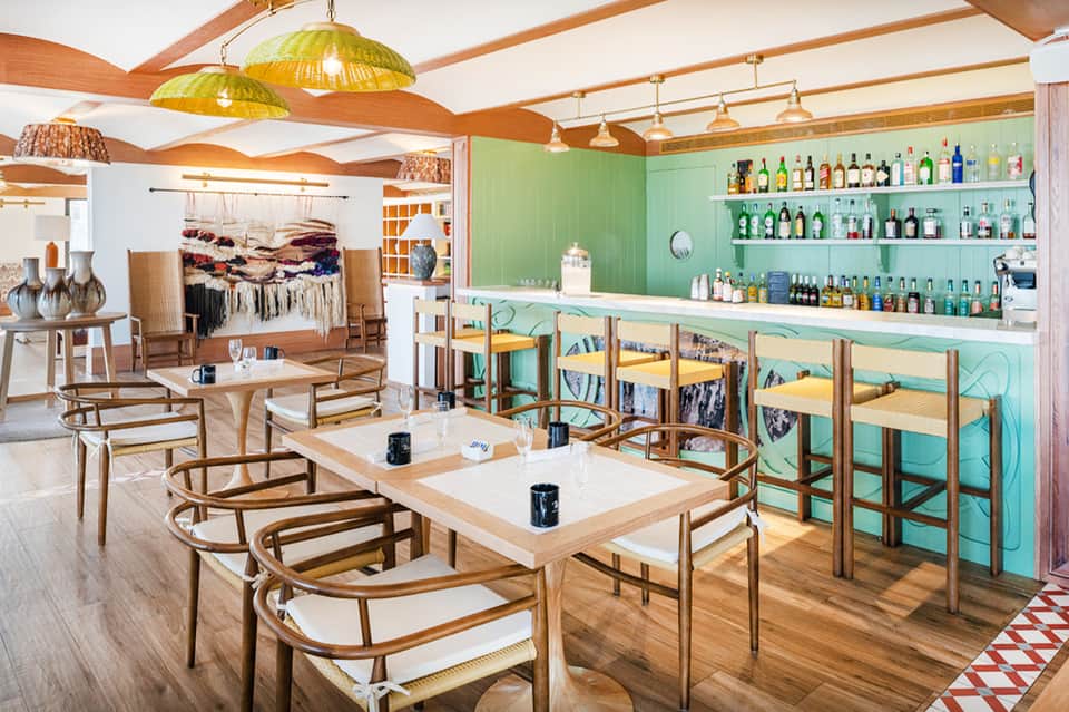 Modern restaurant interior with mint green walls, wooden furniture, brass pendant lights, and full bar