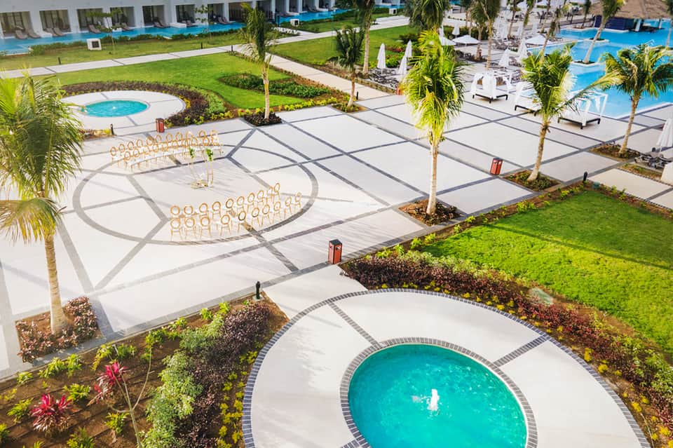 Aerial view of resort grounds with circular pools, white lounge chairs, palm trees, and manicured lawns