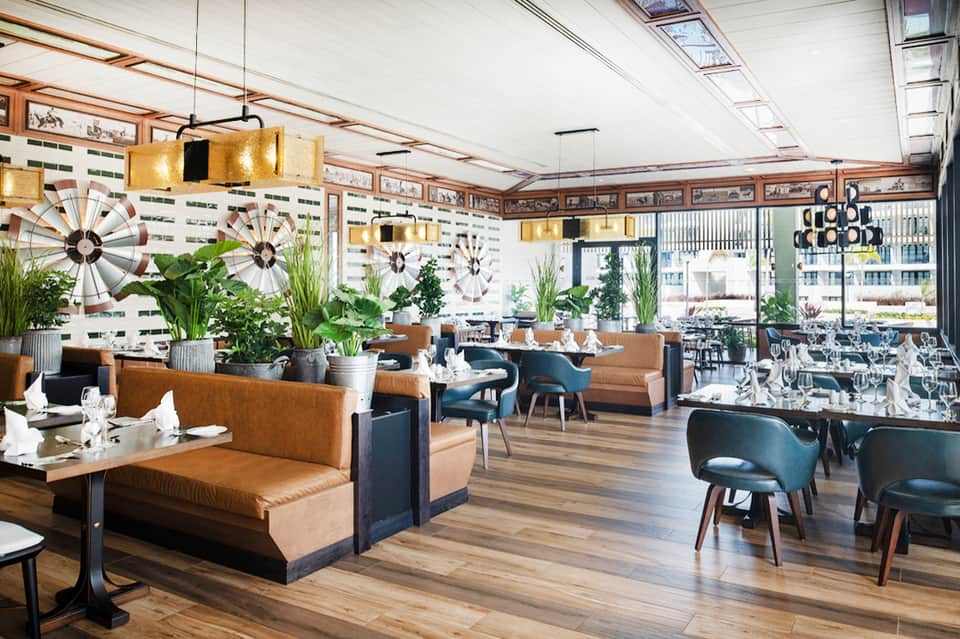 Contemporary restaurant interior with tan banquettes, decorative windmills, and ocean views