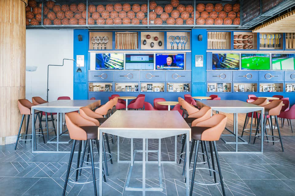 Sports bar lounge with blue storage wall, basketball displays, and high-top tables