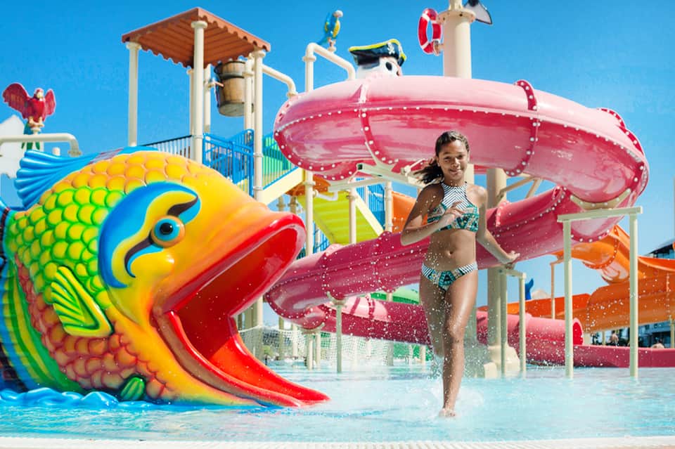Child playing on colorful water slide at aquatic park with tropical-themed playground structures