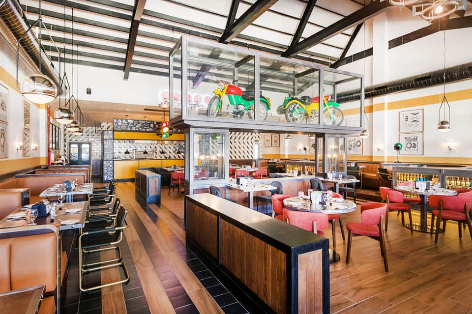Contemporary restaurant with high ceilings, colorful vintage bikes on display, and wooden bar