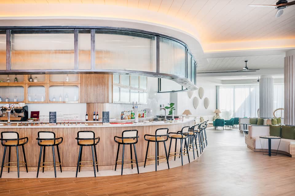 Modern curved bar with wooden cladding, bar stools, and bright open lounge area