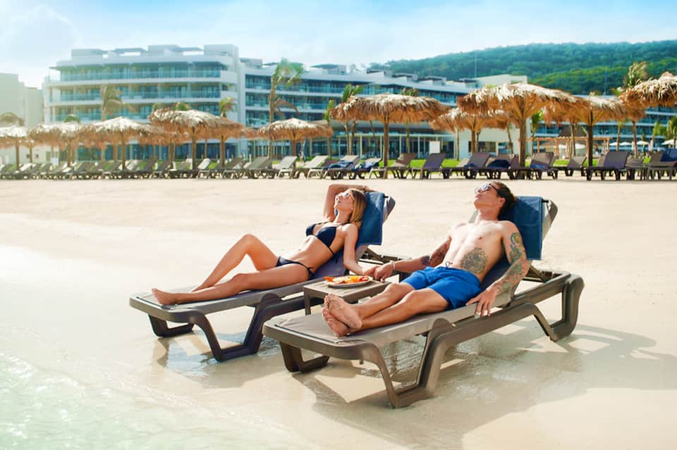 Couple relaxing on lounge chairs in shallow ocean water at beachfront resort