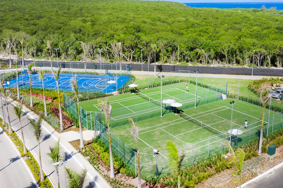 Aerial view of sports complex with blue pickle ball courts, tennis courts, and lush vegetation