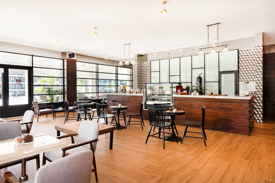 Modern hotel lounge and café with wooden counters, large windows, and mid-century furniture