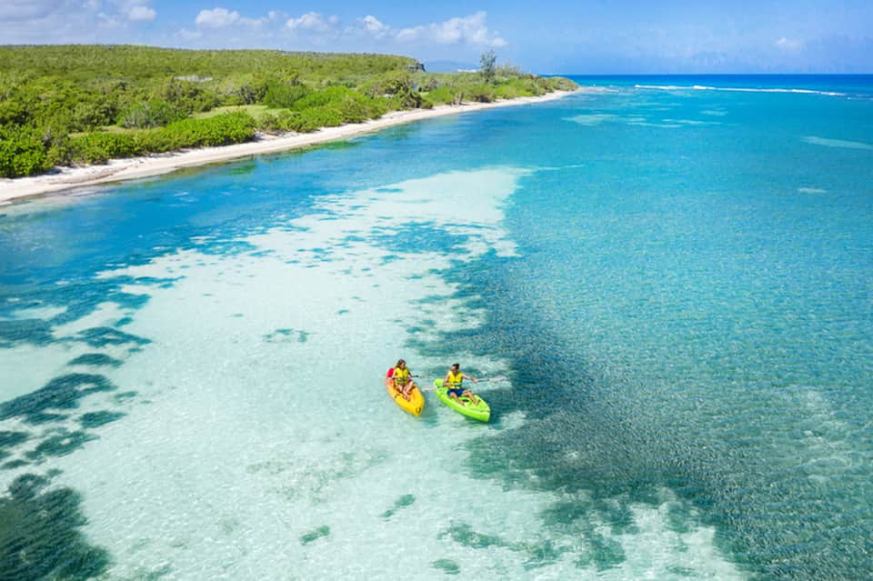 Aerial view of two kayakers in turquoise water with tropical shoreline and lush vegetation