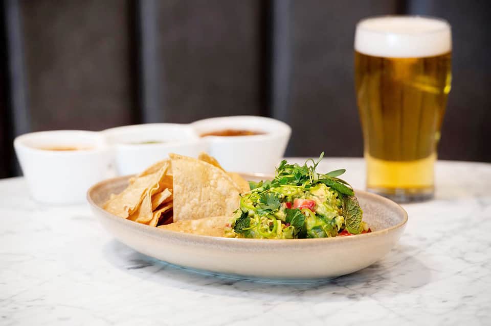 Guacamole and tortilla chips served with beer and coffee cups on marble counter