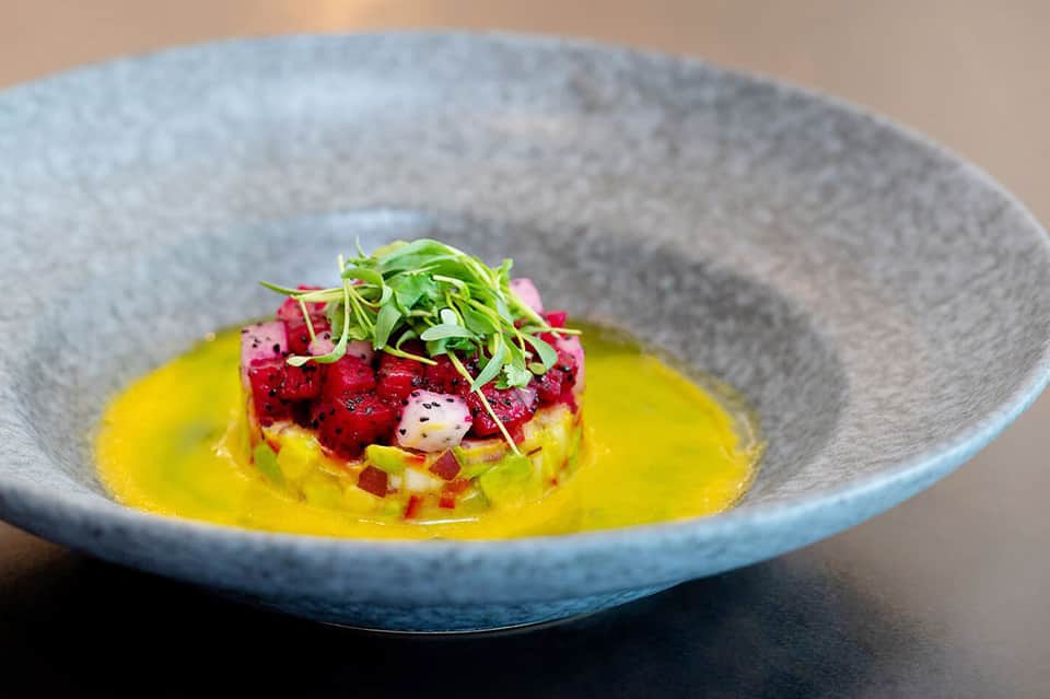 Gourmet dish with red beets, yellow sauce, and microgreens in blue-rimmed bowl