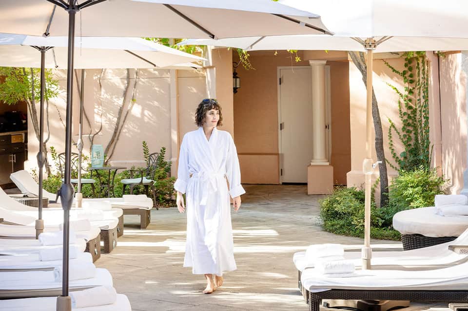 Woman in white robe walking through spa courtyard with lounge chairs and umbrellas