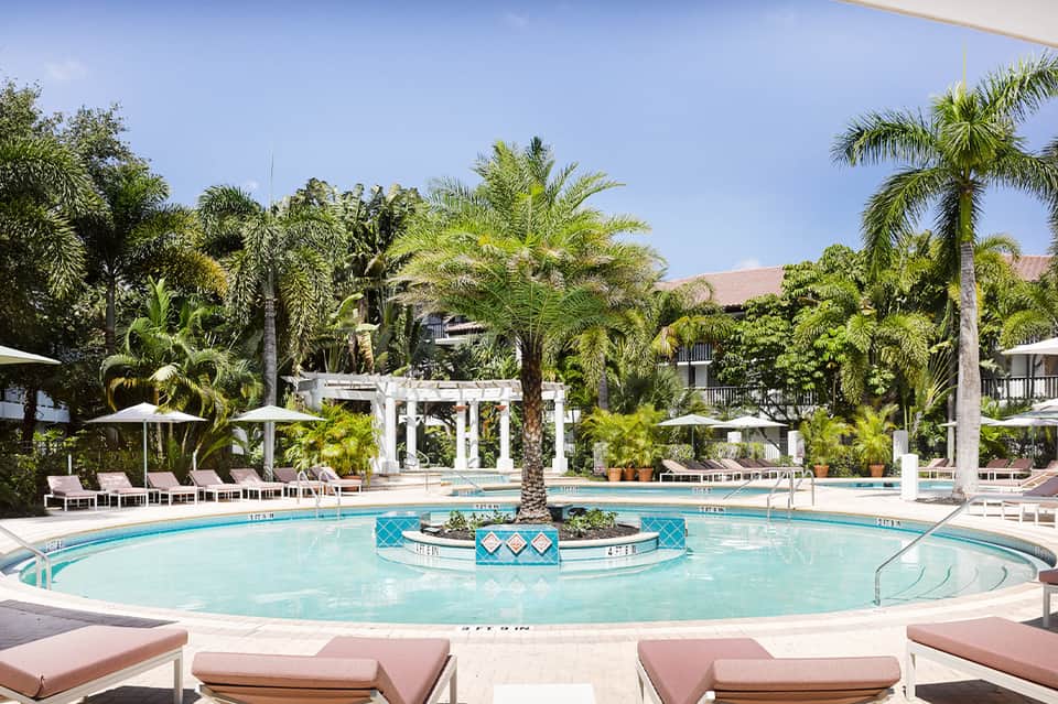 Elegant circular resort pool with palm trees, white umbrellas, and tropical landscaping