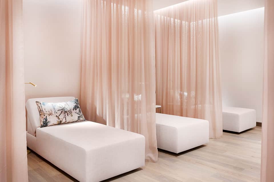 Spa relaxation room with cream chaise lounges separated by flowing pink curtains