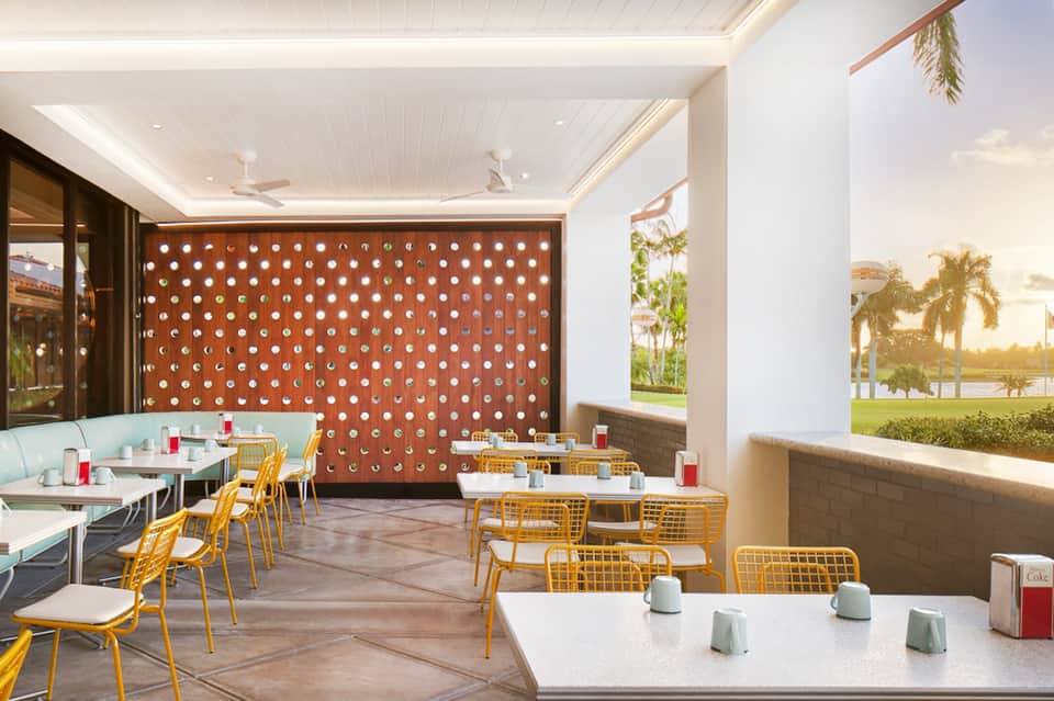 Modern casual dining space with yellow chairs, geometric wall pattern, and panoramic waterfront windows