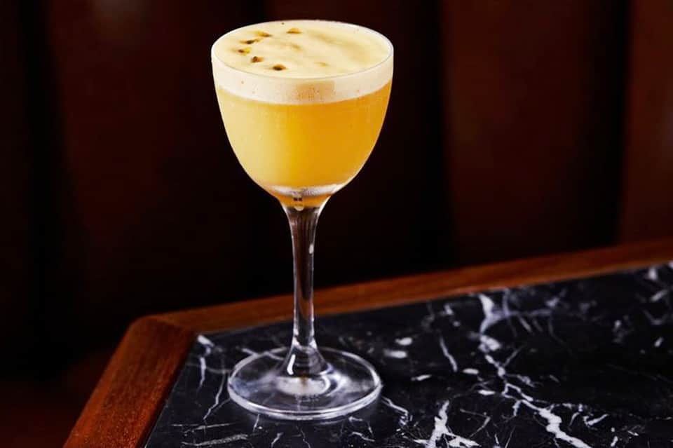 Yellow cocktail with foam topping on dark marble bar counter