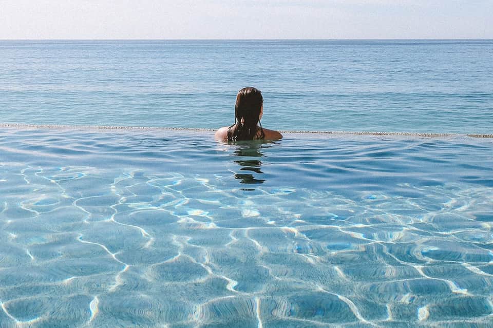Woman swimming in crystal-clear turquoise ocean water with rippled sand patterns visible below