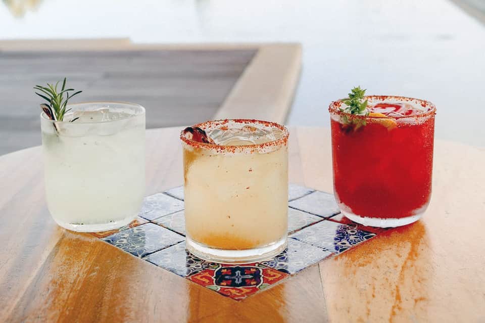 Three colorful cocktails with garnishes on decorative tile at resort bar