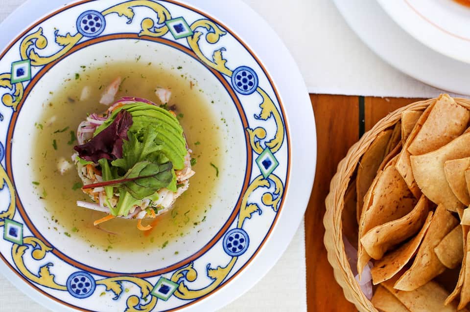 Gourmet soup bowl with decorative blue and yellow rim, fresh greens, and crispy tortilla chips