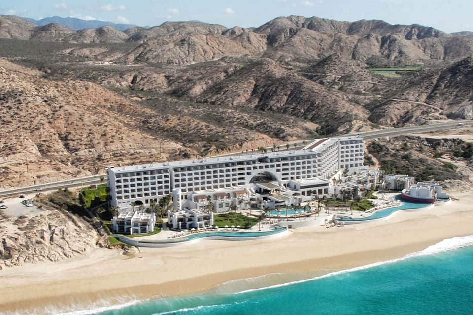 Modern beachfront resort nestled against desert mountains with multiple pools and turquoise water