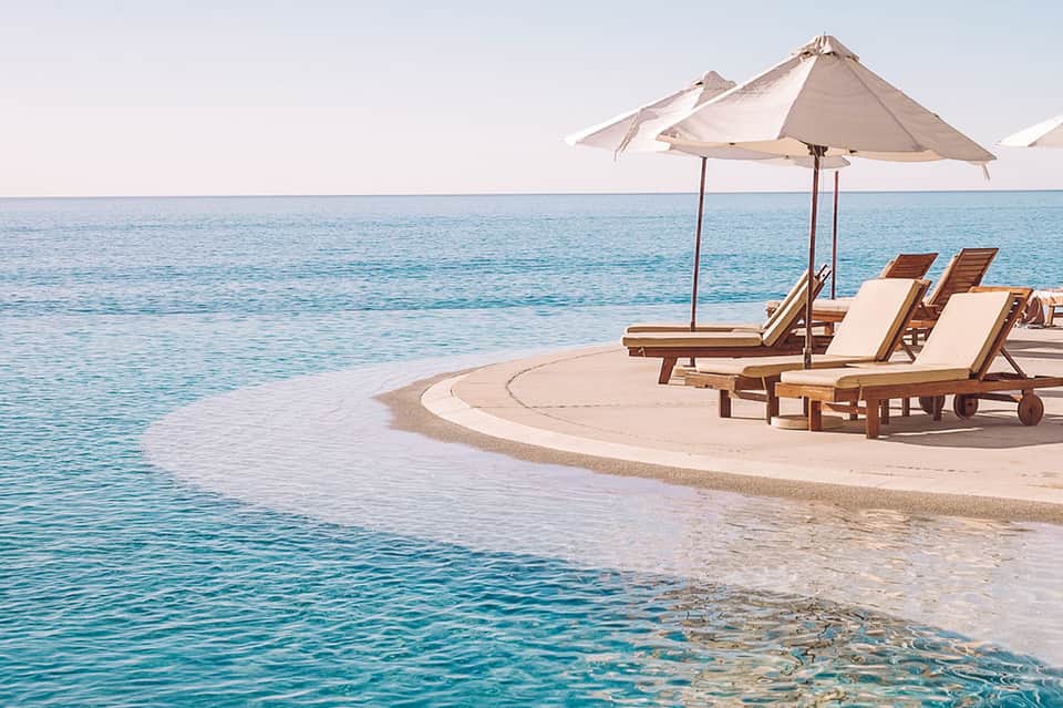 Beach lounge area with wooden sun loungers and white umbrellas on pristine sand