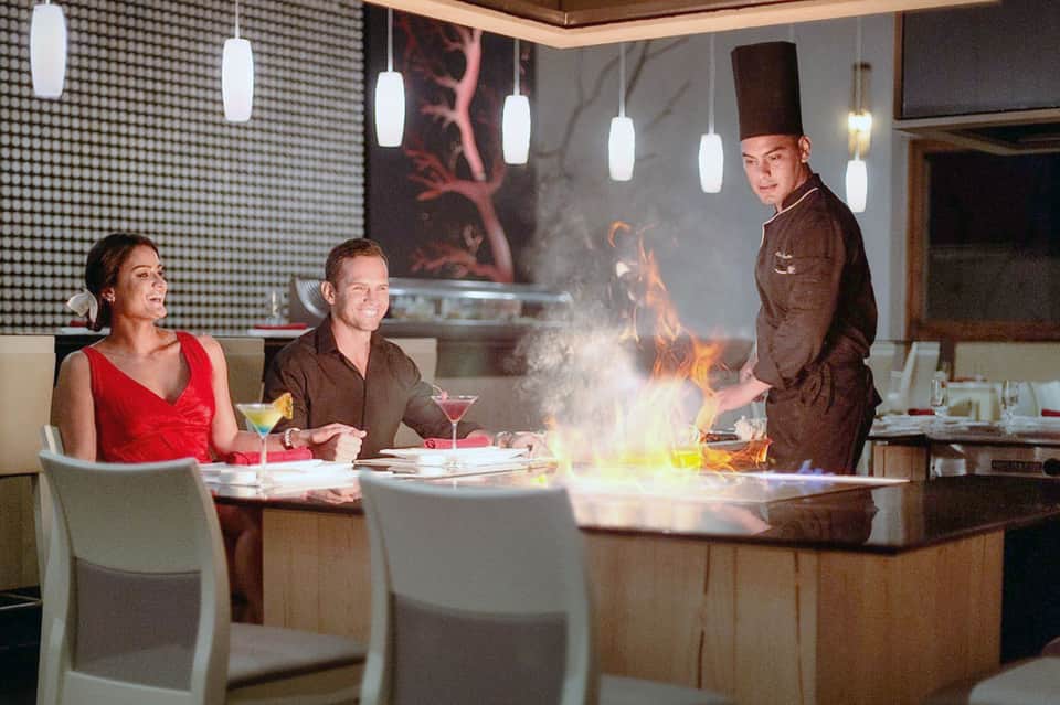 Chef preparing flaming dishes for two diners at an upscale restaurant counter