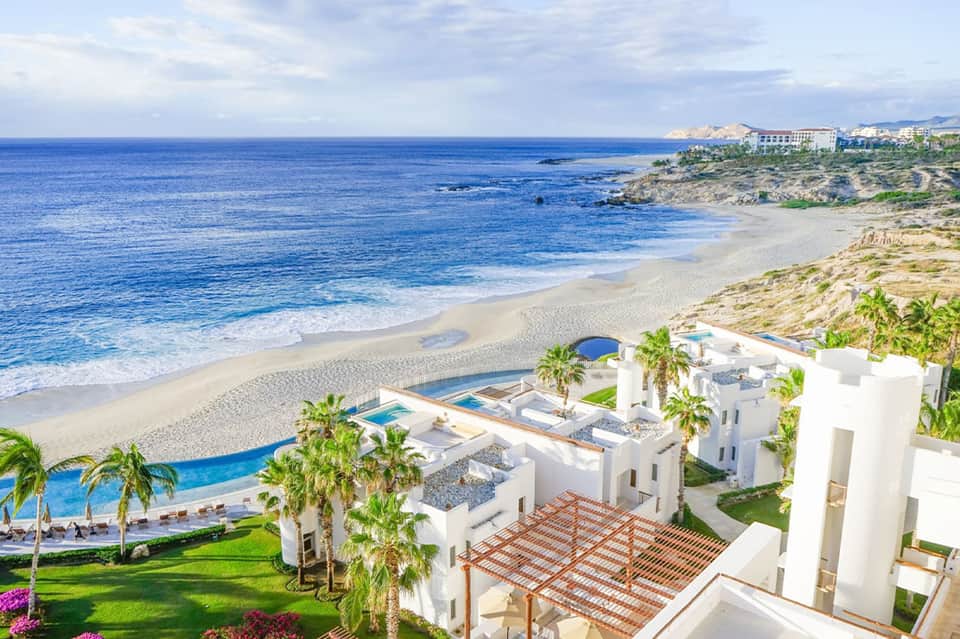 Aerial view of white resort buildings on cliff above sandy beach and ocean