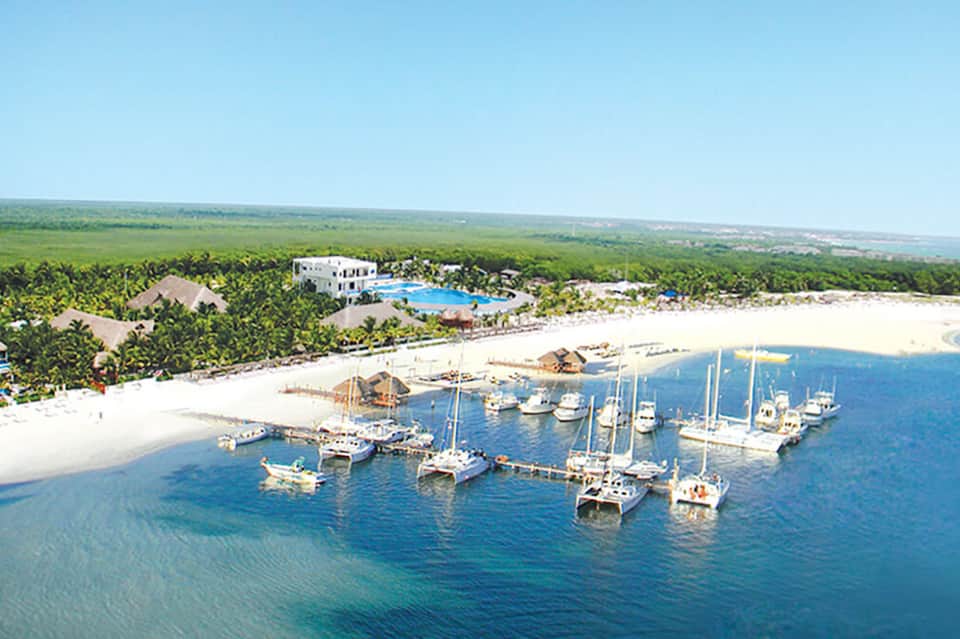 Aerial view of coastal resort with white buildings, pool, boats in marina, and tropical vegetation