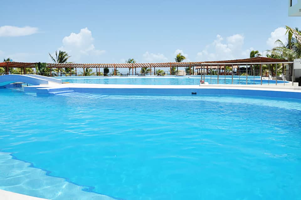 Large bright blue resort swimming pool with palm trees and wooden pergola