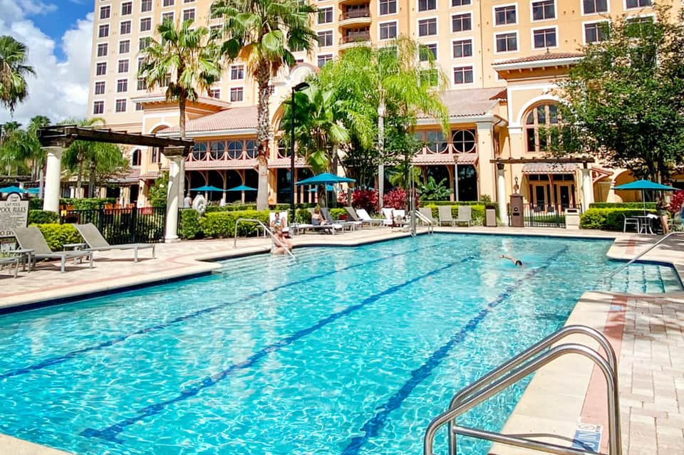 Resort lap pool with lane dividers, lounge chairs, and tropical resort building backdrop