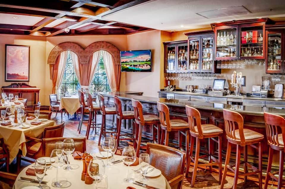 Upscale restaurant interior with arched windows, bar, dining tables, and scenic water views
