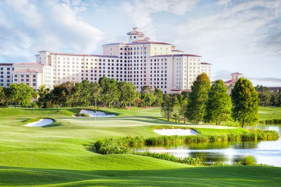 Grand pastel hotel building with clock tower overlooking manicured golf course and water features