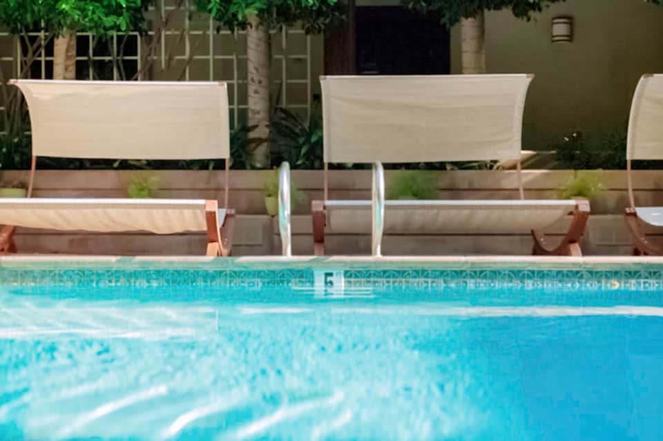 Pool with lounge chairs and cream-colored sun shade panels backed by green garden wall