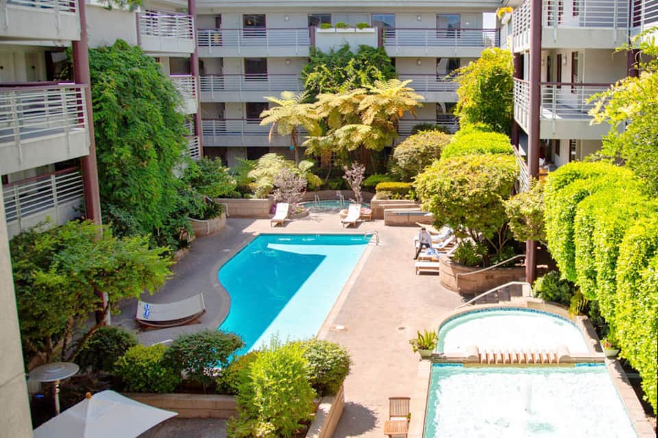 Lush courtyard pool surrounded by tropical plants, apartment buildings with balconies, and manicured landscaping