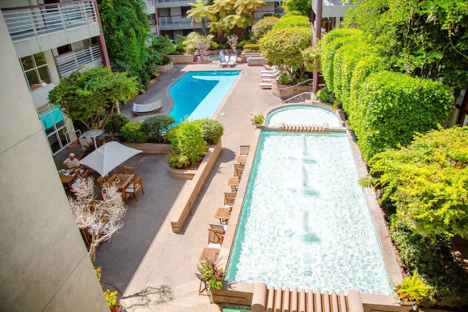 Overhead view of resort courtyard with two lap pools, hot tub, lush greenery, and multi-story building