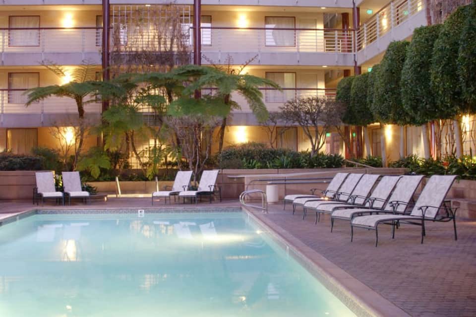 Hotel courtyard pool surrounded by palm trees and lounge chairs with evening lighting