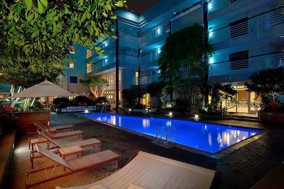 Illuminated courtyard pool at night with glowing blue water, loungers, and modern hotel building