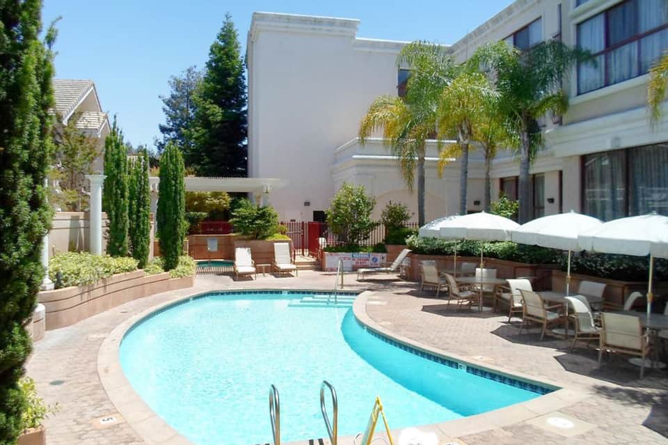 Curved swimming pool with white umbrellas, lounge chairs, and modern resort buildings