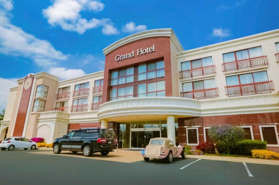 Grand Hotel exterior with red brick and cream-colored facade, parked cars, and landscaping