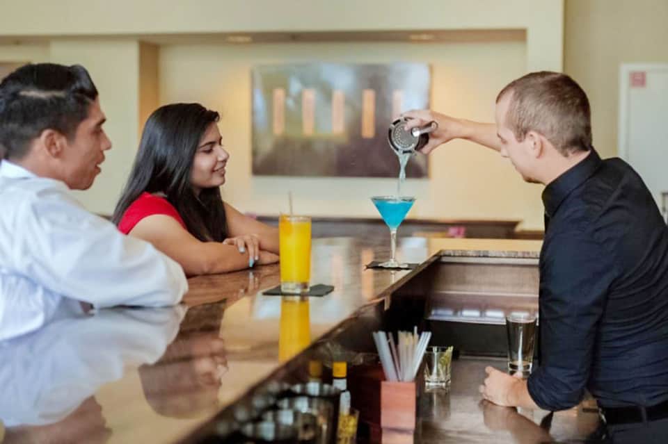 Bartender pouring cocktail for couple at hotel bar counter