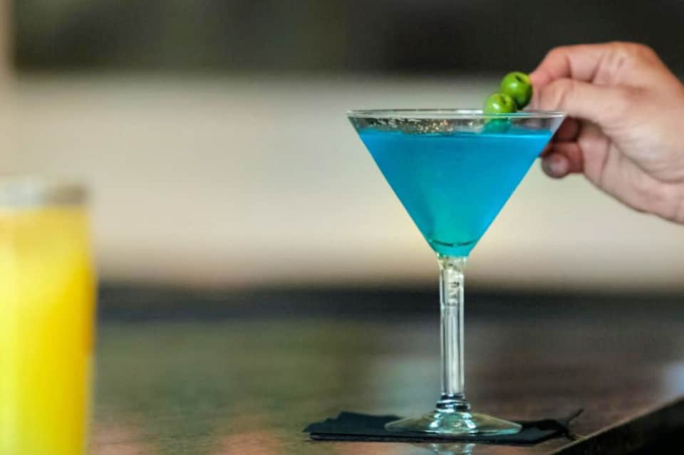 Hand holding blue tropical cocktail with lime garnish and yellow drink beside