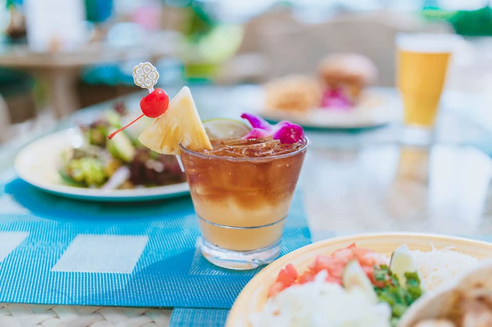 Tropical cocktail with pineapple garnish and appetizers on blue tablecloth