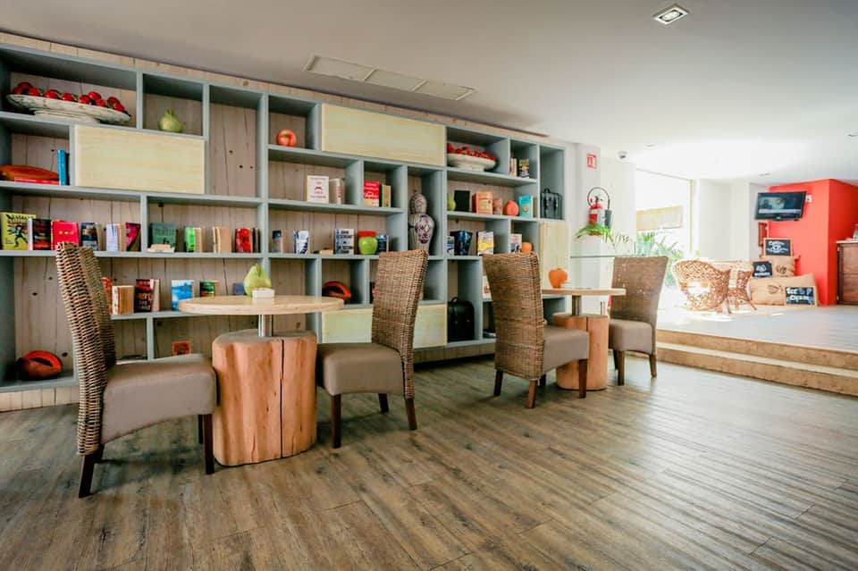 Modern hotel lobby with wooden shelving, wicker chairs, wood tables, and contemporary décor