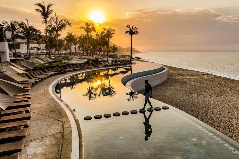 Beachfront resort at golden sunset with curved pool, lounge chairs, and ocean view
