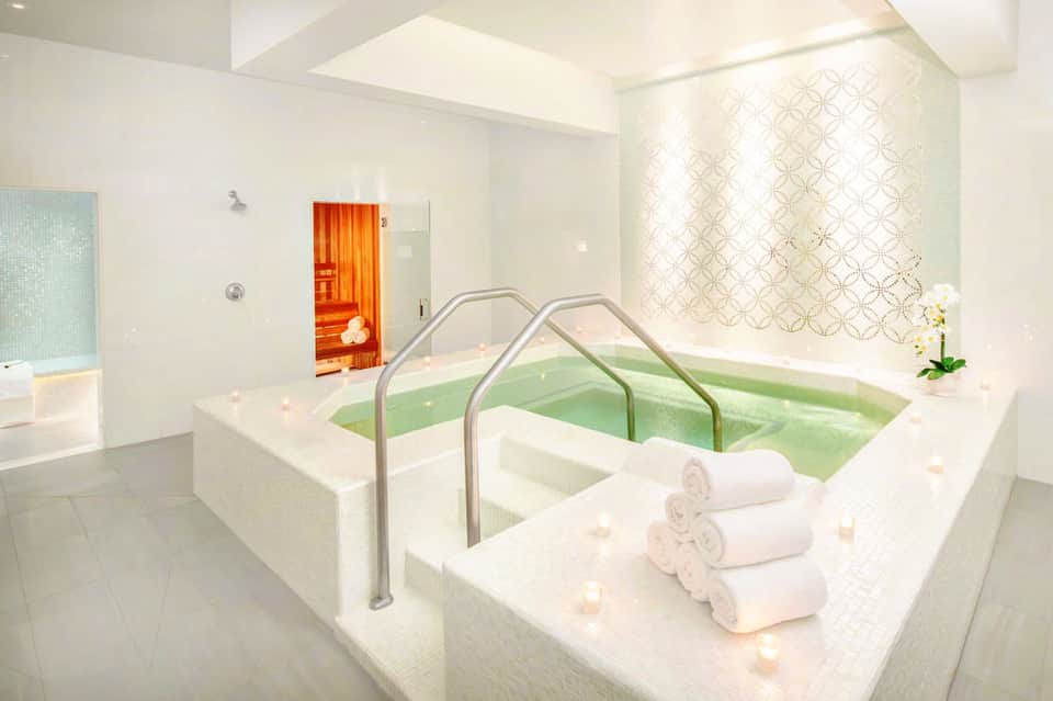 Spa hot tub with green water and rolled white towels, sauna door visible in background