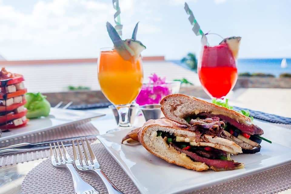 Colorful tropical cocktails and fish tacos with lime garnish served beachside with ocean view