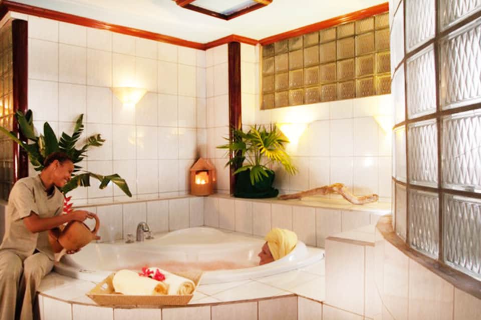 Spa attendant preparing hot tub with tropical plants and tiled bathroom surroundings