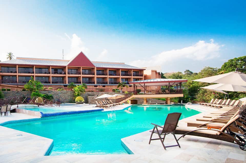Resort pool with turquoise water, brick hotel building, white umbrellas, and surrounding landscaping