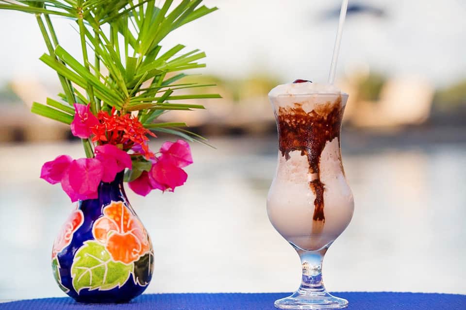 Tropical cocktail with colorful flower vase garnish overlooking beach scenery