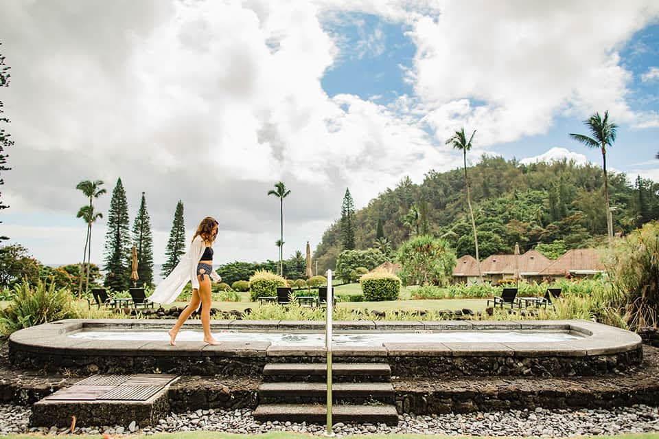 Woman in white wrap walking near a modern circular soaking pool with tropical vegetation